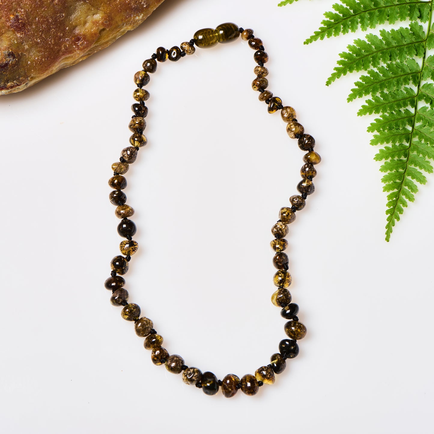 a shiny polished green amber beaded necklace, displayed in between a rock and a fern