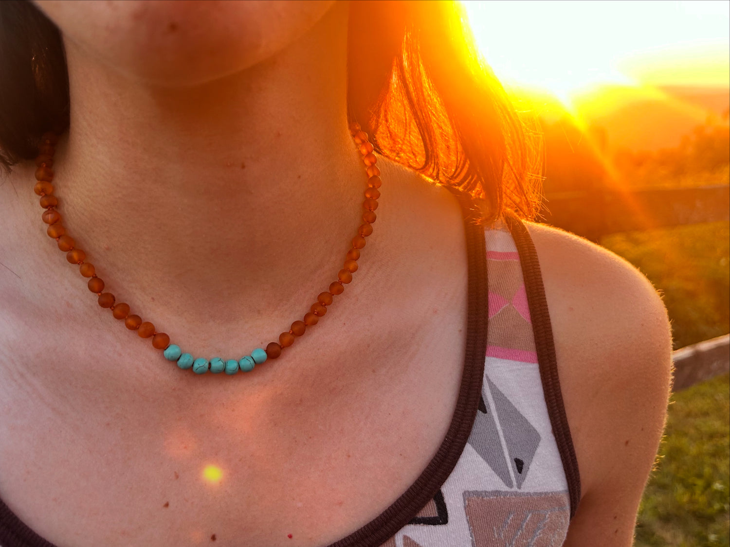 close up photo of a young woman wearing a raw amber and turquoise necklace at sunset