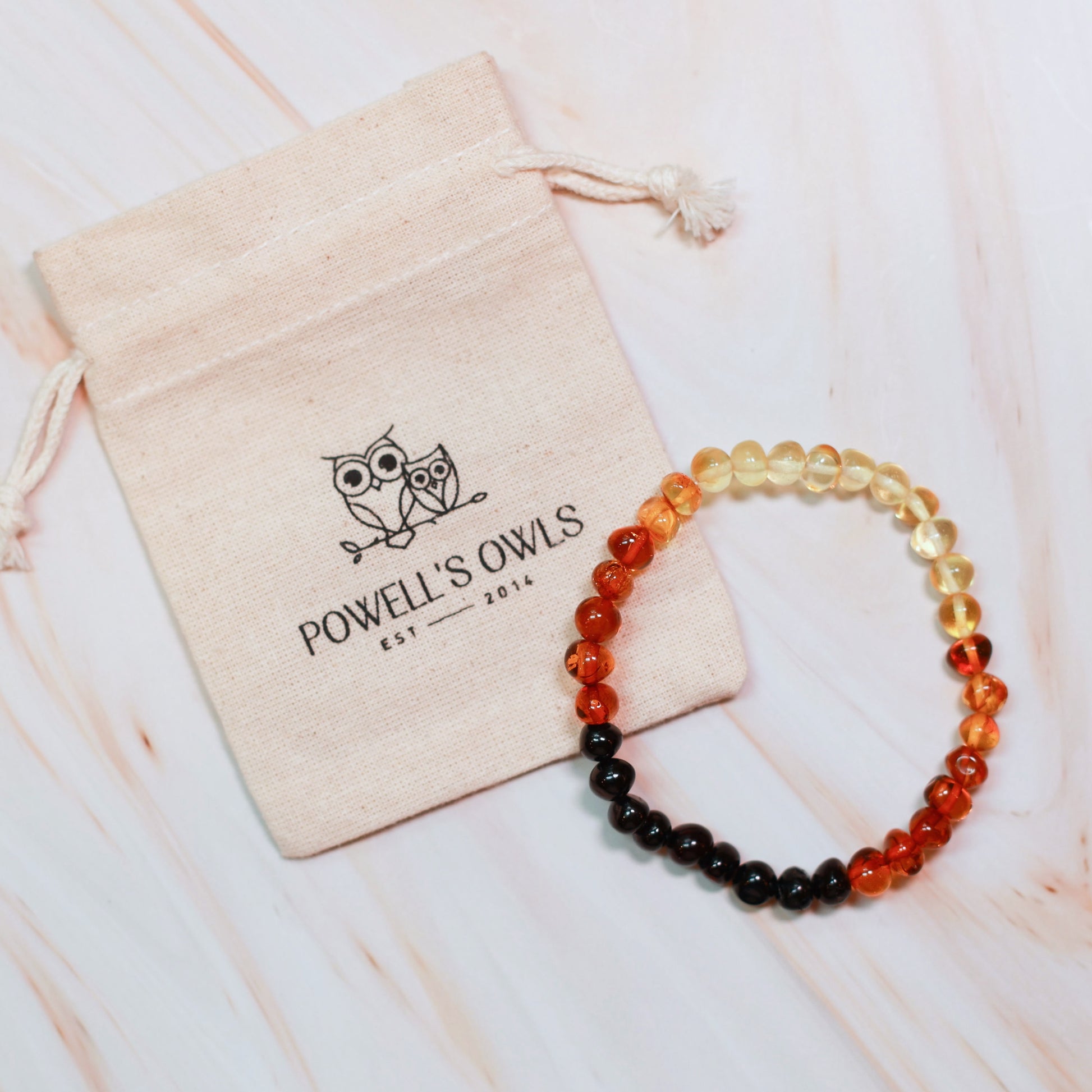 Beaded amber bracelet on a light textured surface with a branded Powell's Owls cotton jewelry pouch