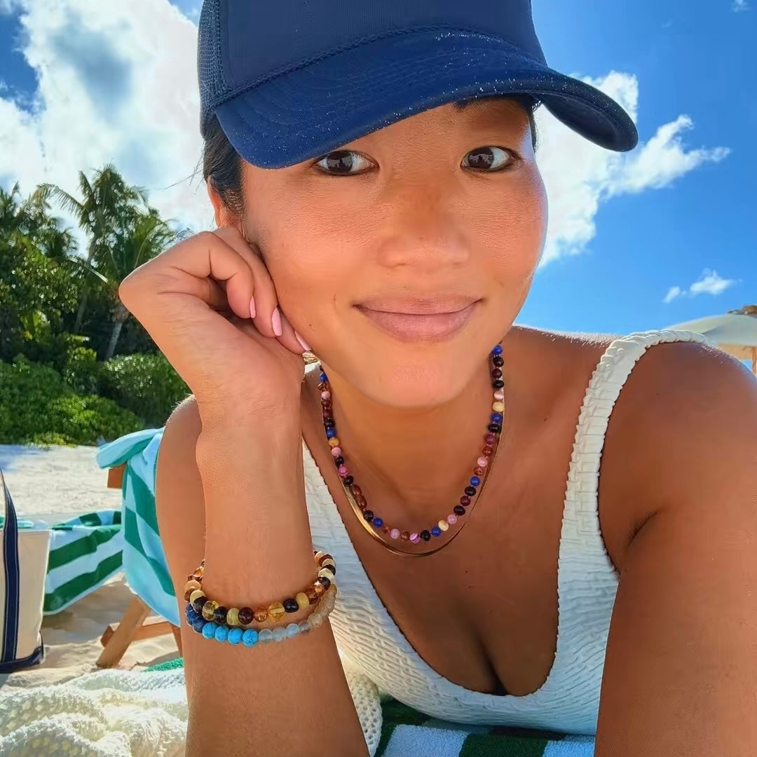 adult woman in a hat wearing multicolored baltic amber necklaces and bracelets on a beach