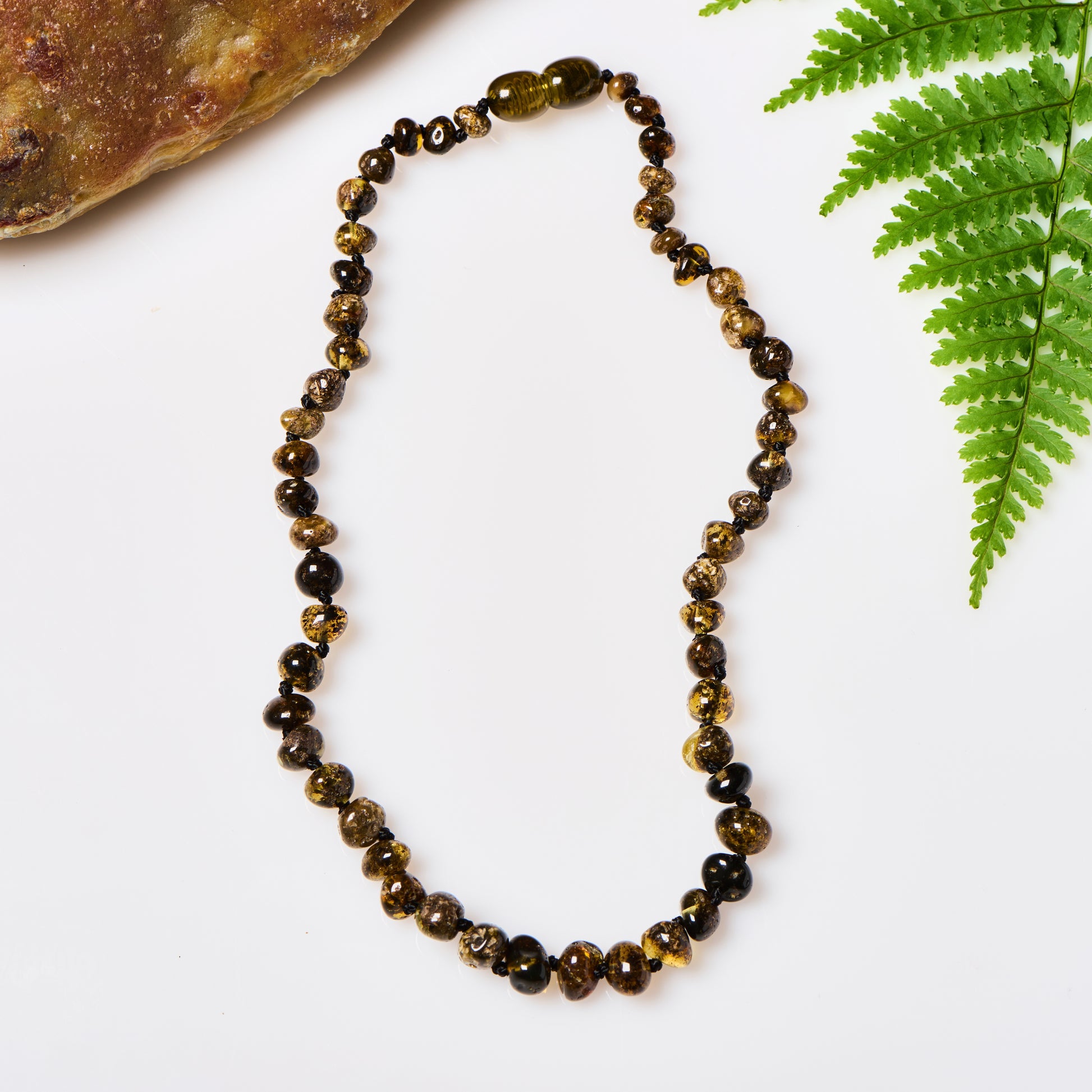 a shiny polished green amber beaded necklace, displayed in between a rock and a fern