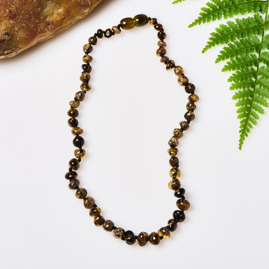 a shiny polished green amber beaded necklace, displayed in between a rock and a fern
