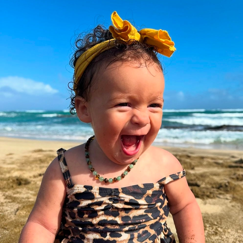 laughing toddler on a beach wearing a green amber and agate teething necklace