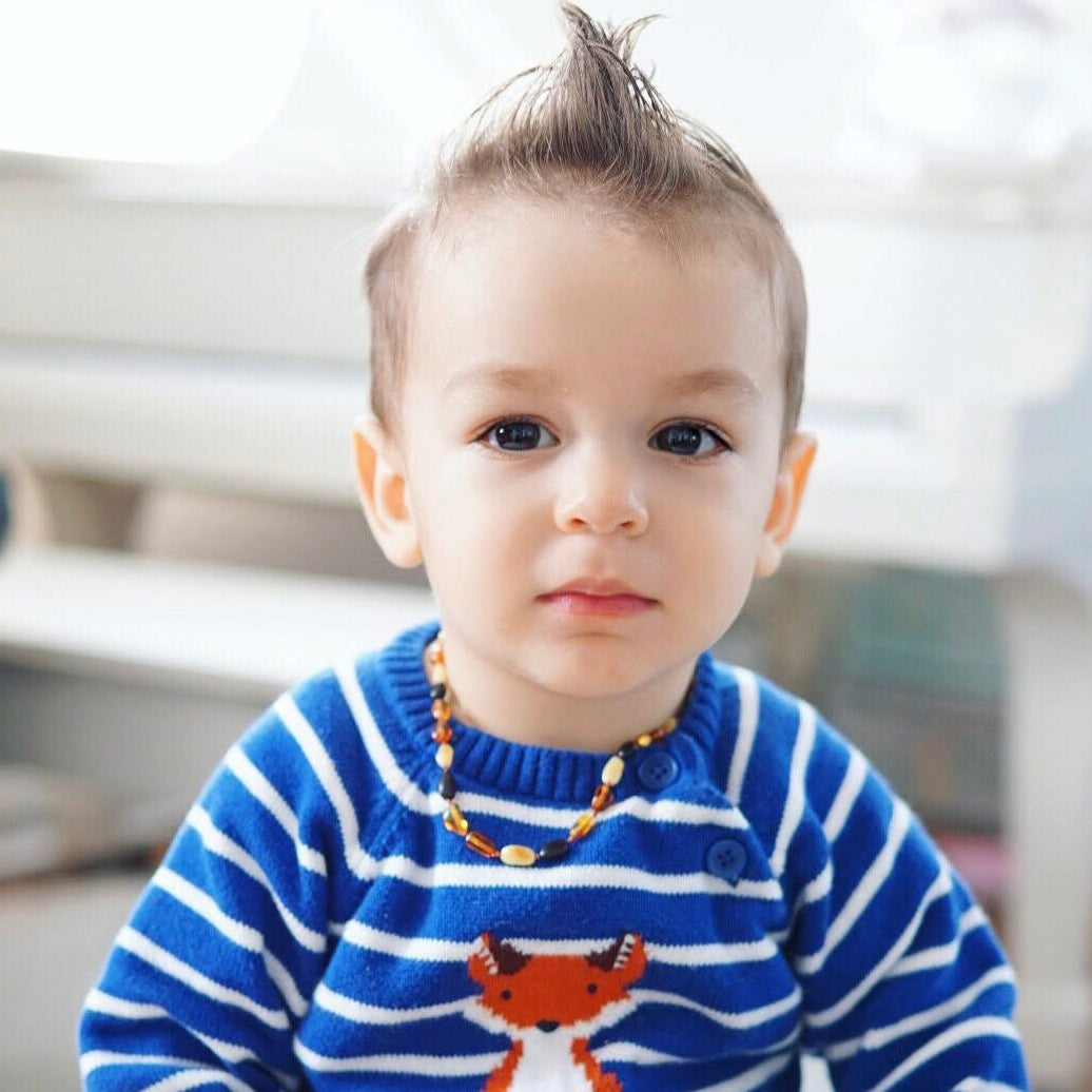 toddler child wearing a multicolor amber beaded teething necklace in a blue and white striped sweater with a fox design